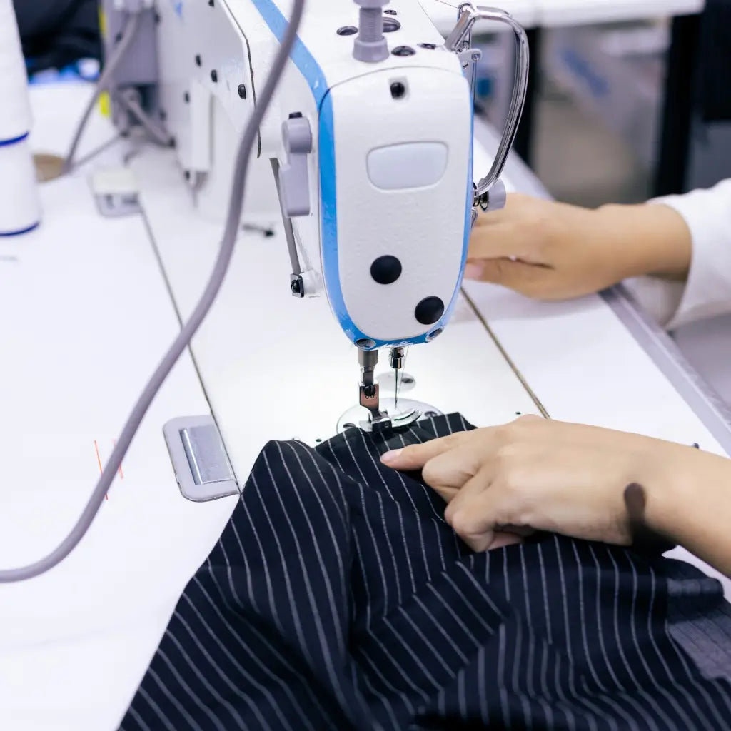 Person using a sewing machine on striped fabric in a workshop setting